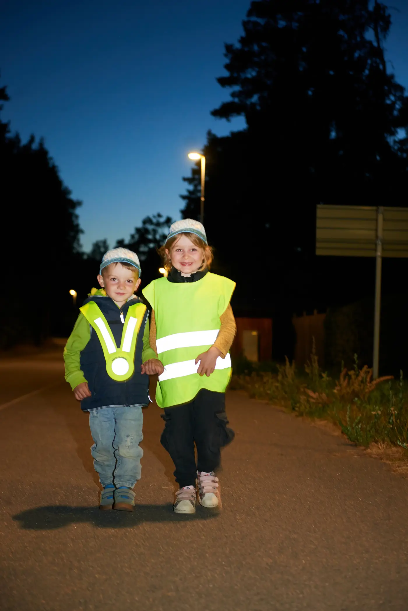 Två barn med reflexväst på gångbana i mörker.