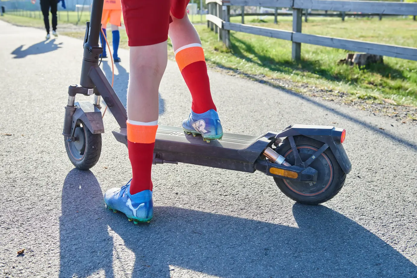 Ett barn med fotbollskläder sår med ena foten på en elsparkcykel.